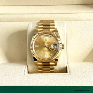 Close-up of gold dial with stick markers and day window at twelve