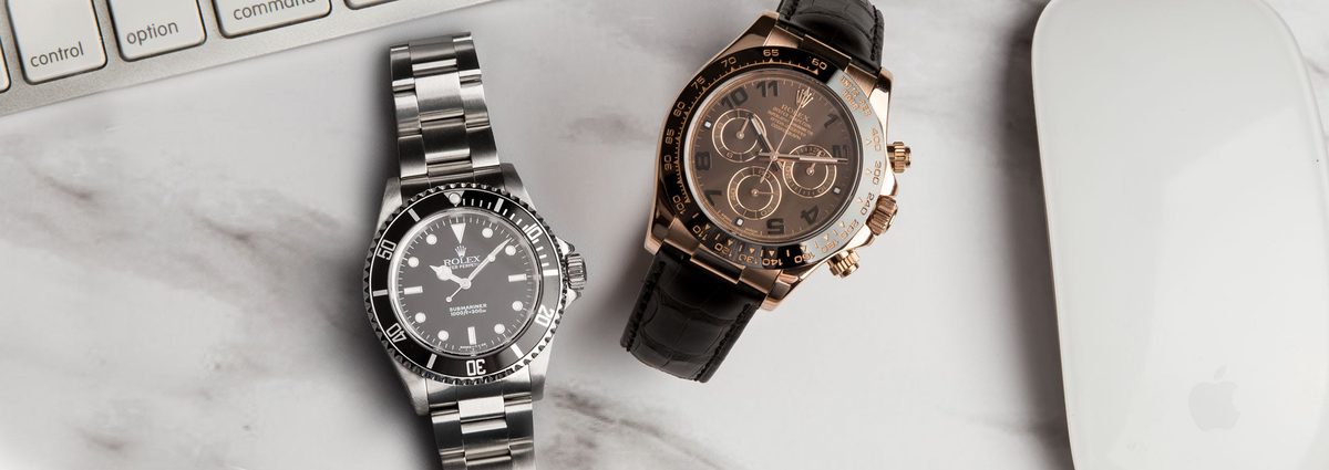 Rolex Submariner steel and Daytona rose gold side by side flat lay on marble desk
