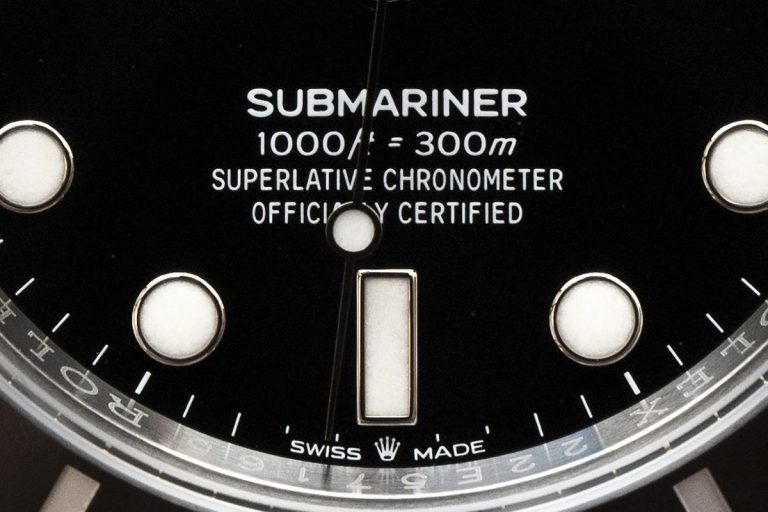 Rolex Submariner dial macro showing SUBMARINER text, lume markers, rehaut engraving and SWISS MADE crown
